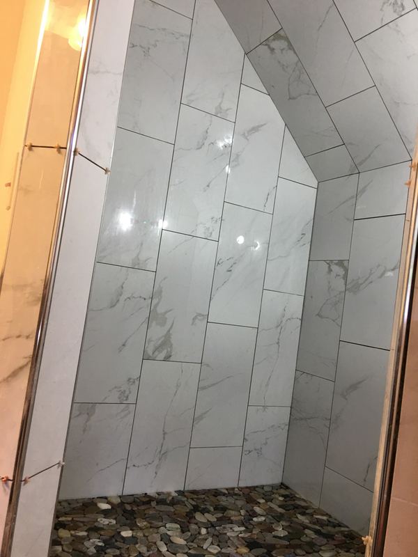 Marble-look shower under a sloped ceiling with a river-rock pebble floor.