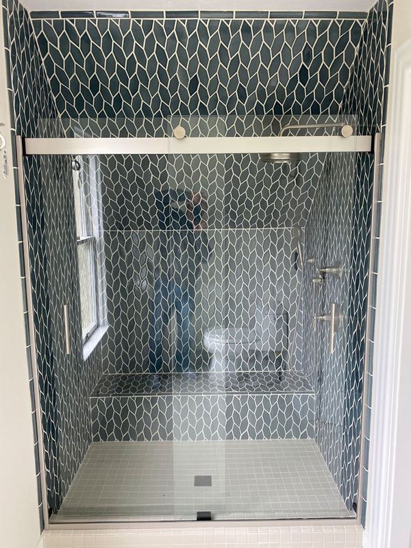 Glass-door shower lined with patterned tile and a marble-look surround.