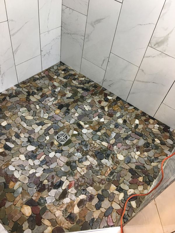 River-rock pebble shower floor set tight against large marble wall tile.