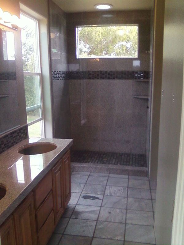 Bathroom floor in stone-look tile running under a vanity into a walk-in shower.