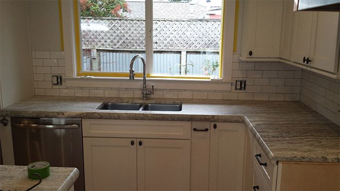 White kitchen with a travertine backsplash and tiled counter.