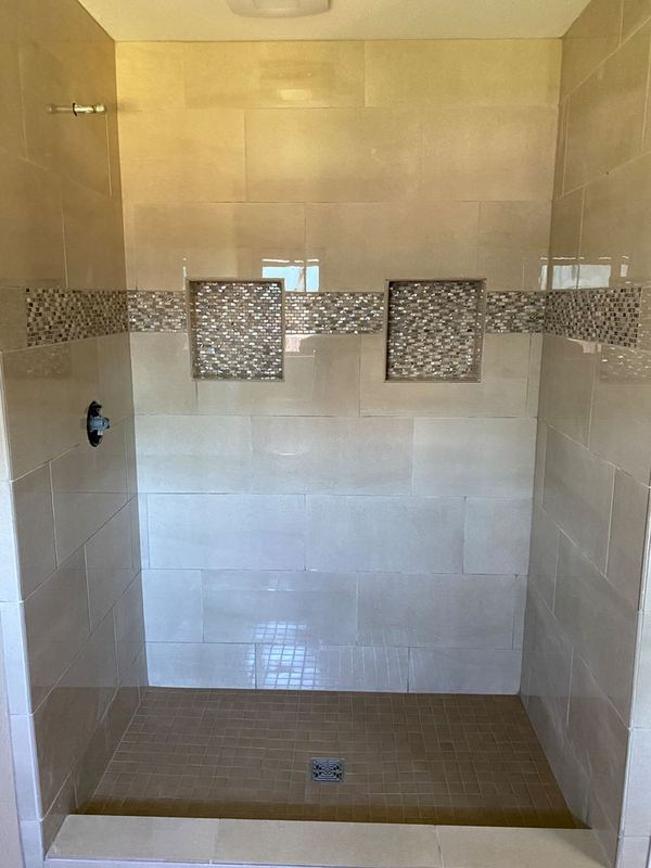 Walk-in shower in cream large-format tile with two inset accent squares and a built-in bench.