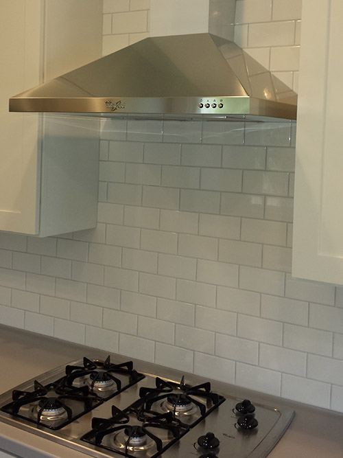 White subway-tile backsplash behind a gas range and stainless hood.